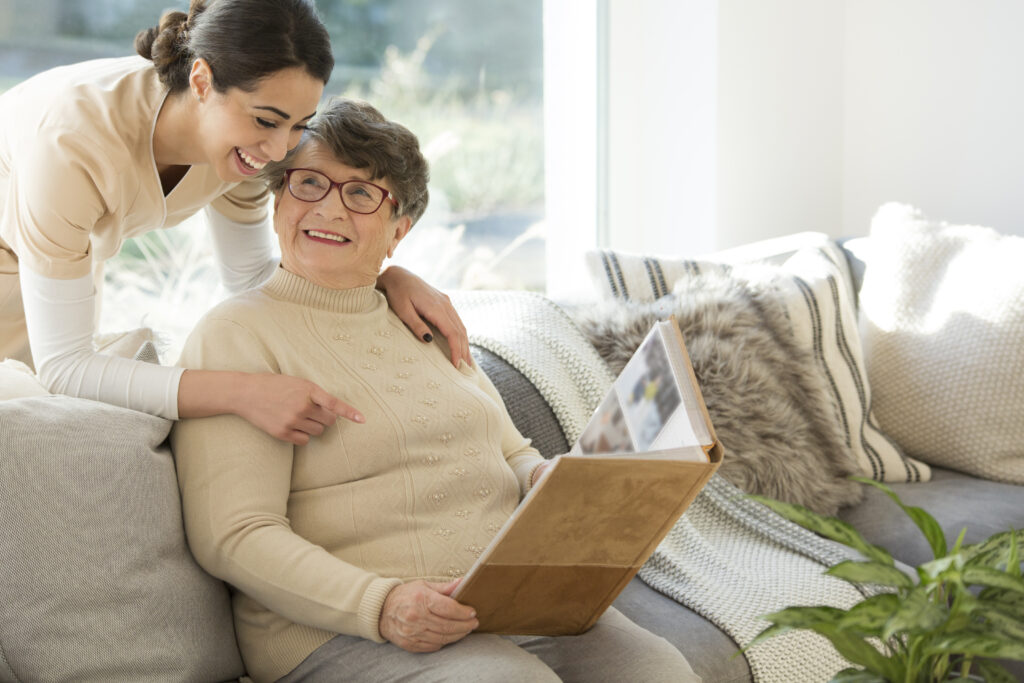 Grandmother sitting on a couch in a sunny room, looking at a photo album and sharing fond memories with a tender caregiver